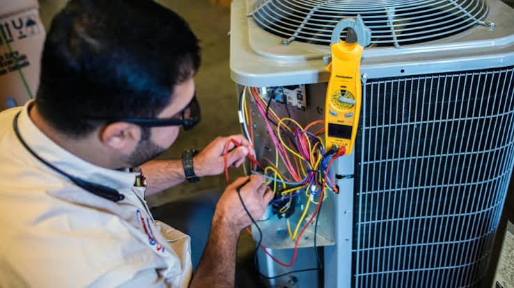 Technician testing electrical connections in an outdoor air conditioner