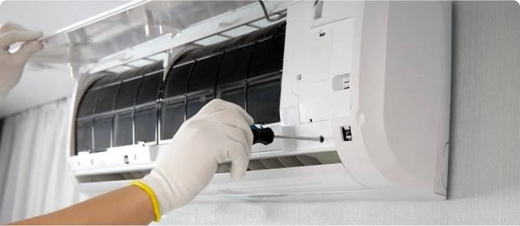 Gloved hands servicing the filters of a wall-mounted indoor air conditioner