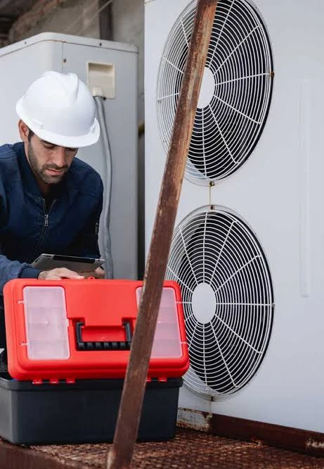 HVAC technician using a tablet beside an outdoor heating and cooling unit